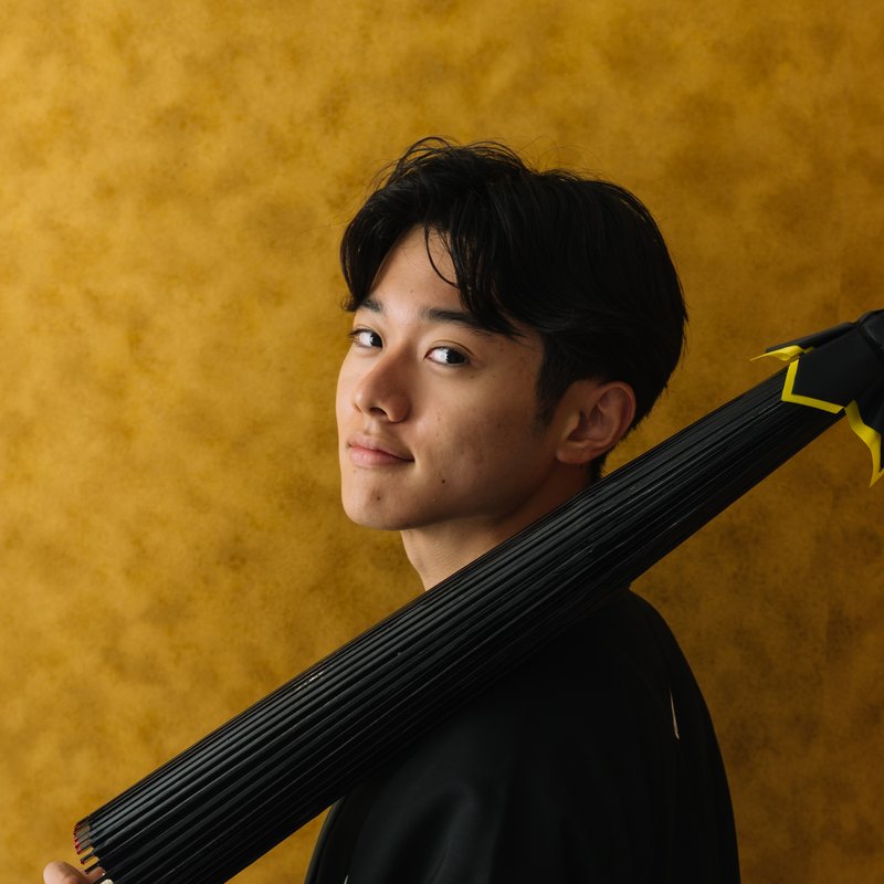 Jin Soma, in a black kimono against a gold background